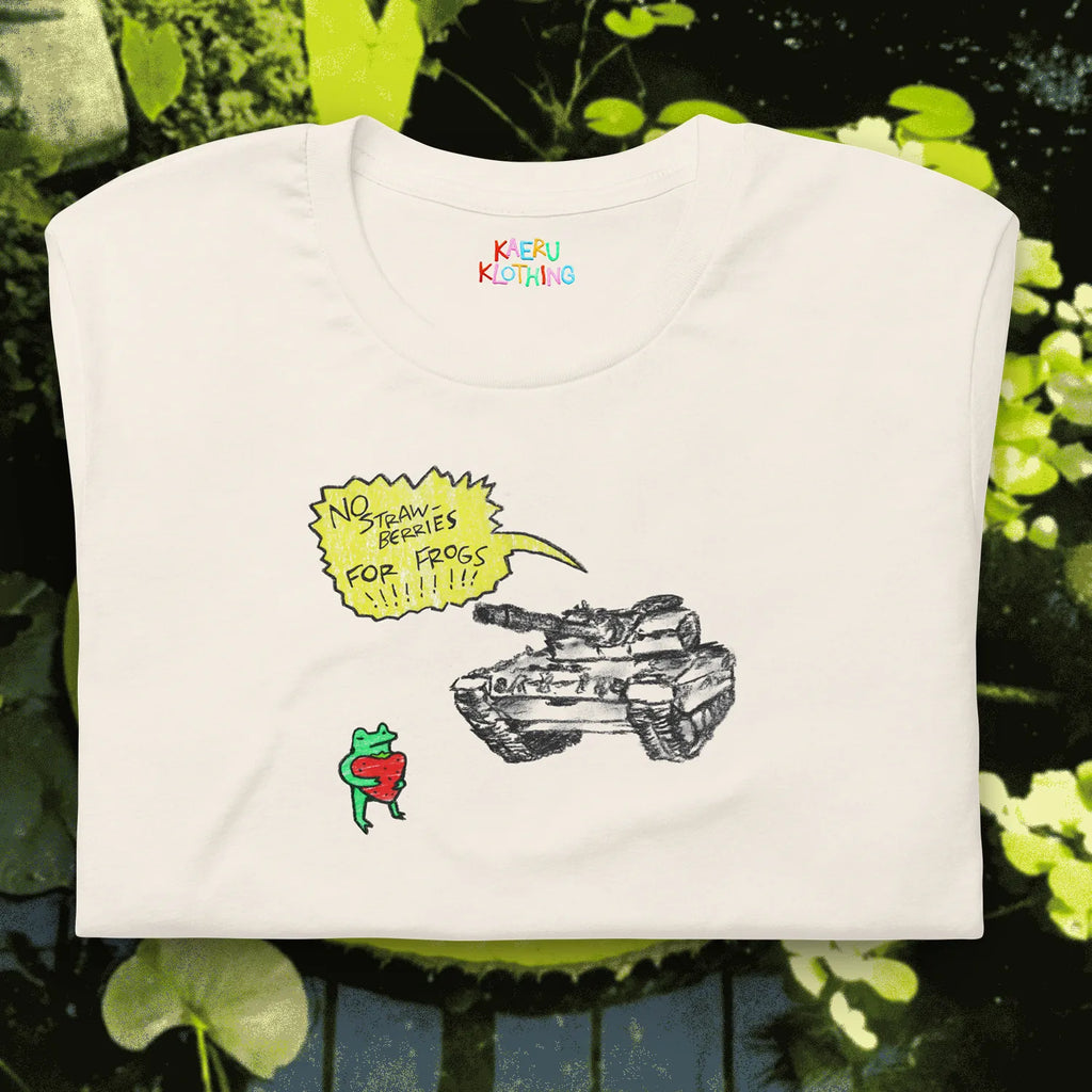TANKRU TEE by Kaeru Klothing — white unisex cotton tee, folded, featuring hand-drawn frog design: frog holding a strawberry in front of a tank with a yellow speech bubble saying “NO STRAWBERRIES FOR FROGS.”