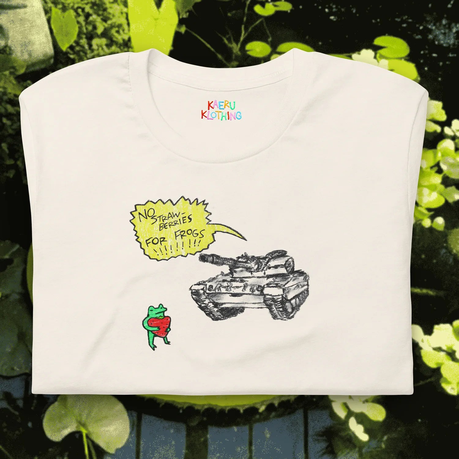 TANKRU TEE by Kaeru Klothing — white unisex cotton tee, folded, featuring hand-drawn frog design: frog holding a strawberry in front of a tank with a yellow speech bubble saying “NO STRAWBERRIES FOR FROGS.”
